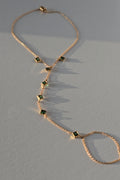 A gold hand chain with emeralds on a warm gray surface