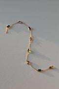 A delicate gold chain bracelet featuring alternating rectangular green emerald-cut stones and marquise-cut clear crystals, displayed on a neutral light gray background.