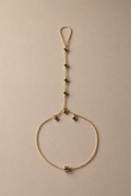 Delicate gold hand chain with green gemstones on a beige background