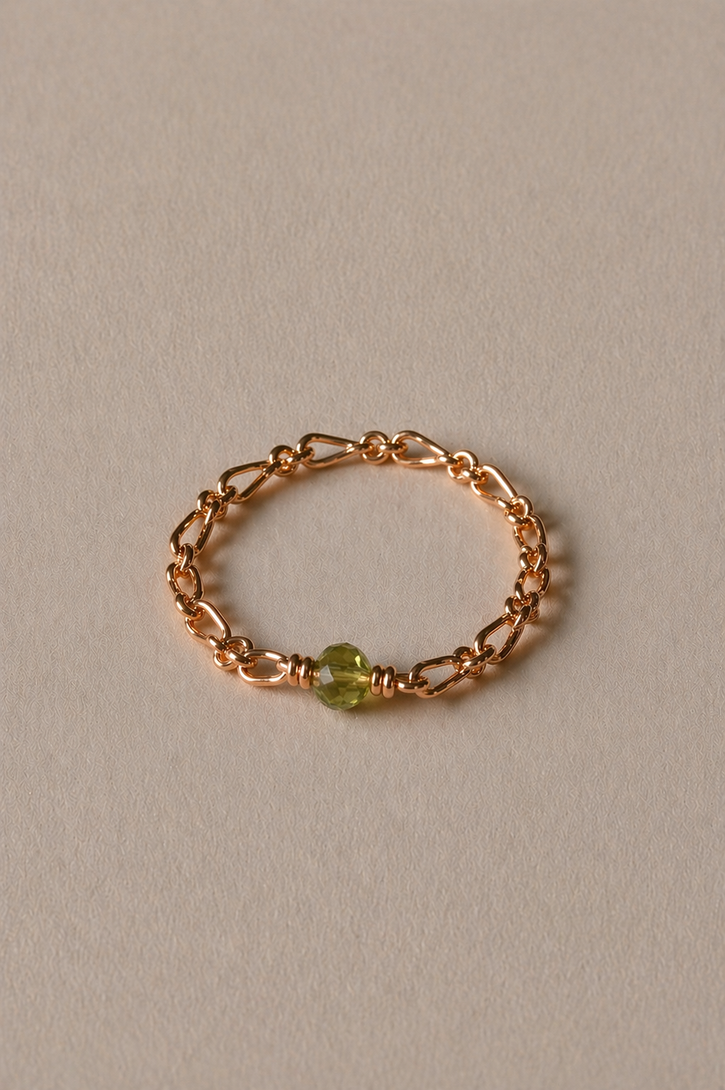 Gold chain bracelet with a peridot bead on a beige background