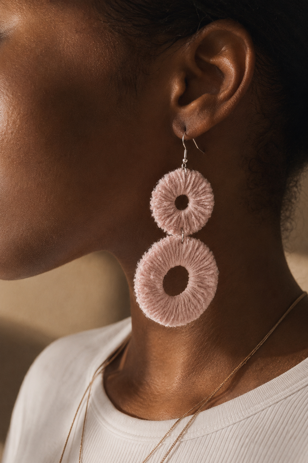 Close-up of a person wearing pink circular velvet earrings with a blurred background