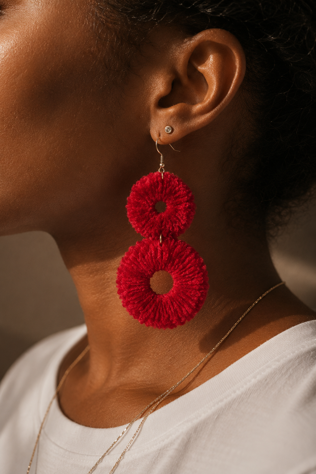 Close-up of a person wearing red pom-pom velvet earrings with a neutral background