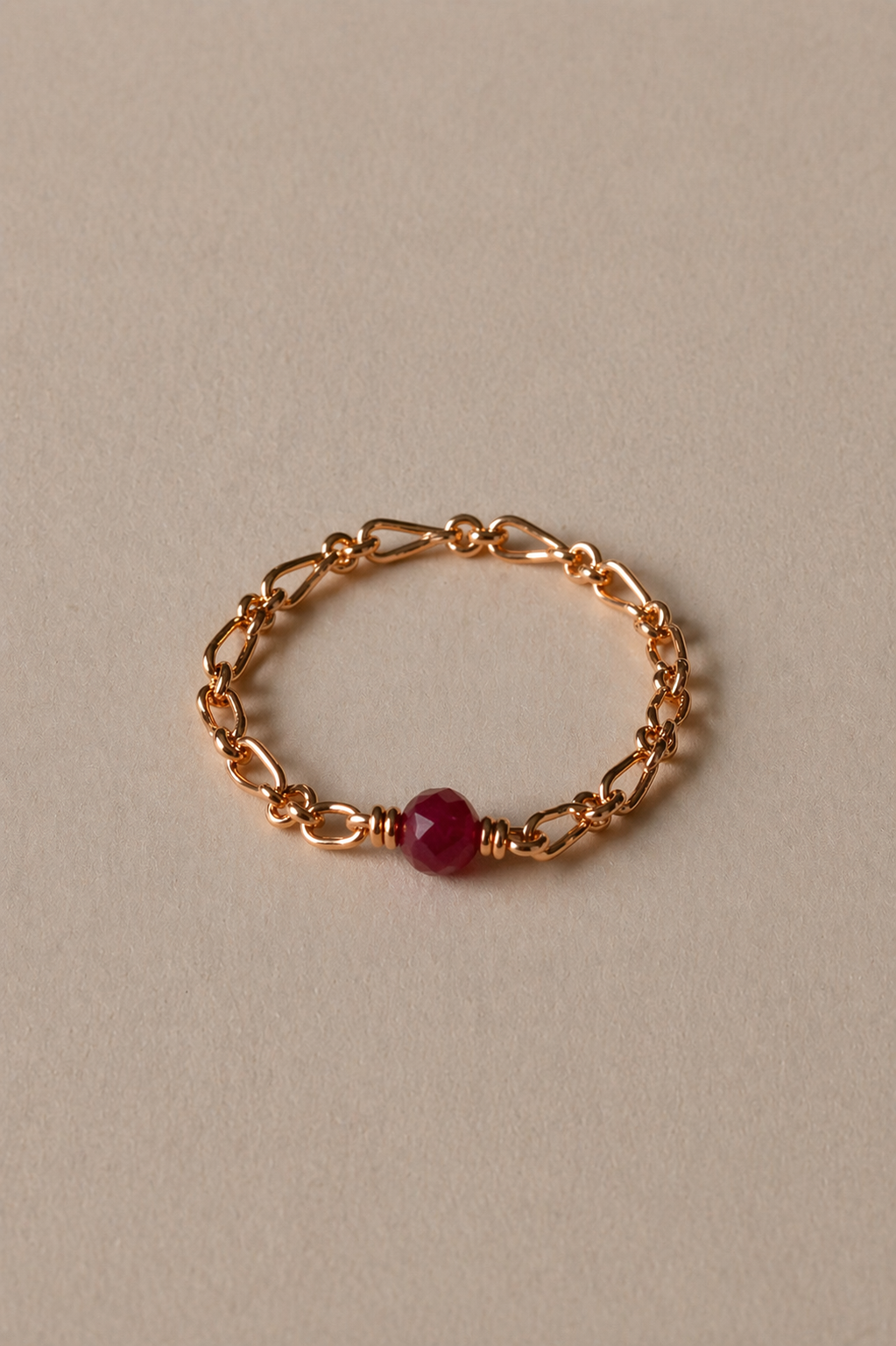 Gold chain bracelet with a ruby gemstone on a beige background