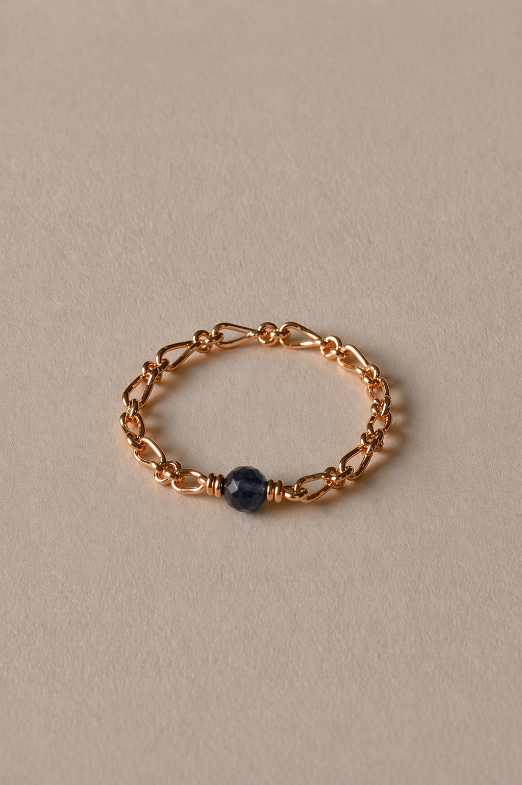 Gold chain bracelet with a sapphire bead on a beige background