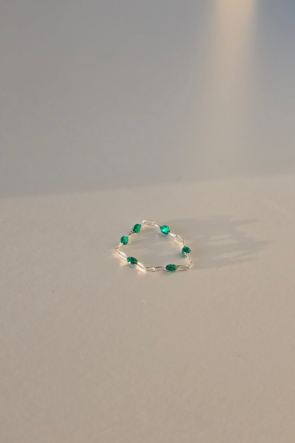A delicate silver ring featuring a circular arrangement of small green gemstones, shown against a plain light gray background.