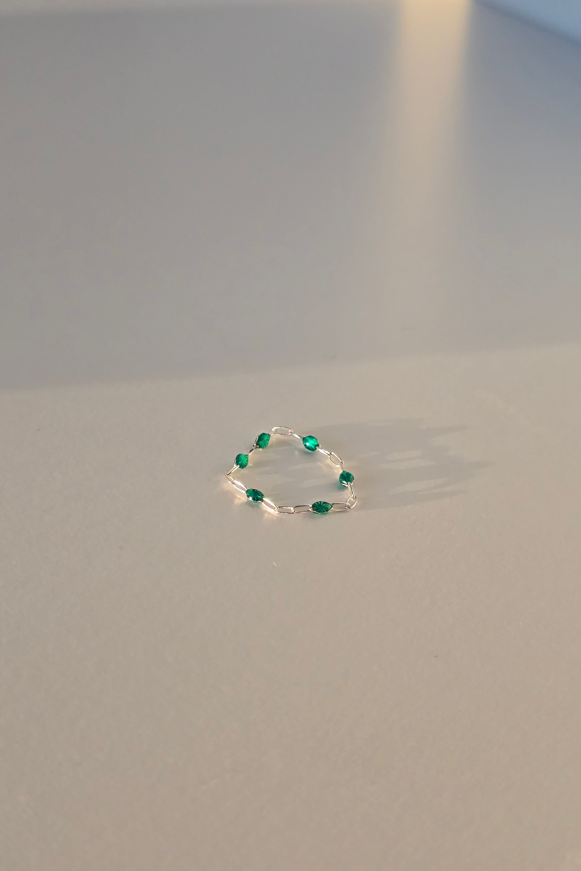 A delicate silver ring featuring a circular arrangement of small green gemstones, shown against a plain light gray background.