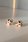 A pair of round gold-toned stud earrings with a cream-colored enamel face, decorated with multiple colorful gemstones in green, pink, purple, and orange, resting on a light gray surface.