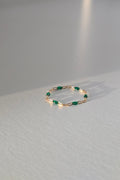 A delicate gold ring with small green gemstone accents, lasting on a light gray textured table.