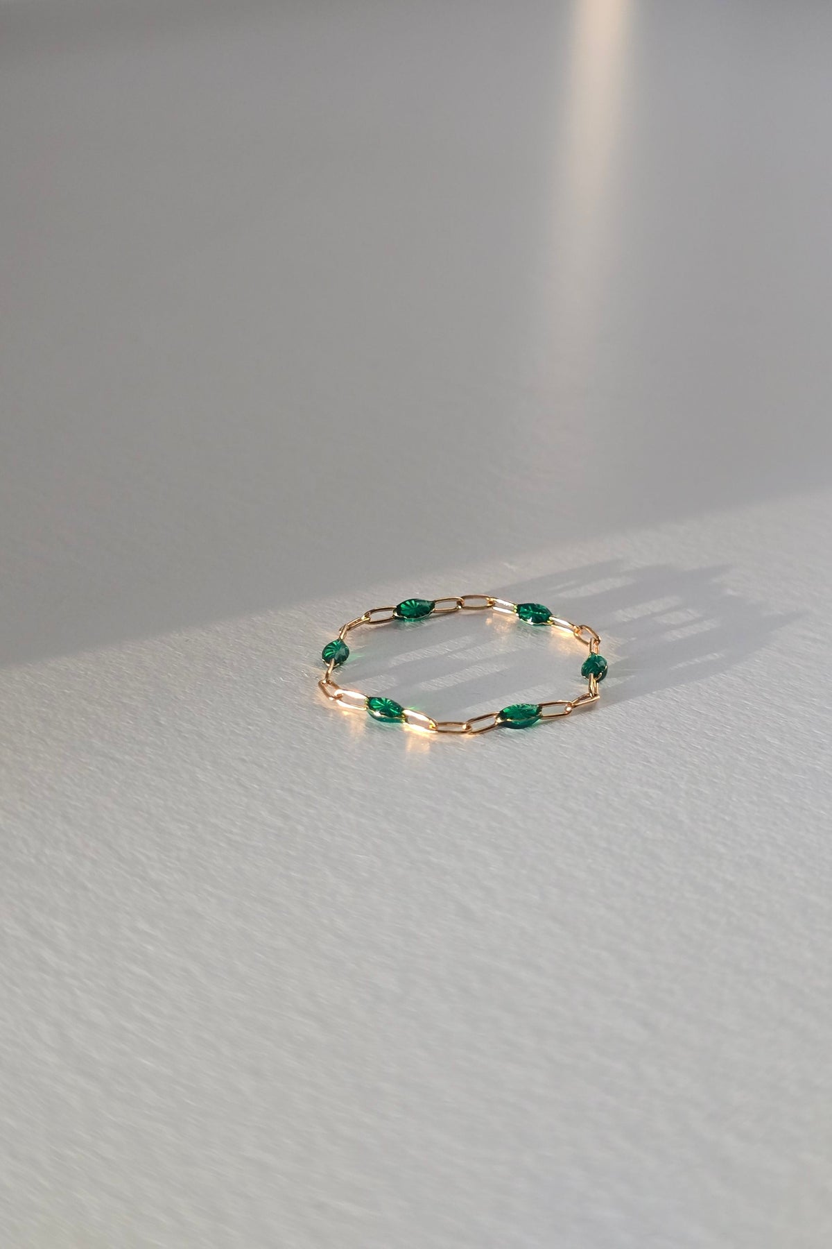 A delicate gold ring with small green gemstone accents, lasting on a light gray textured table.