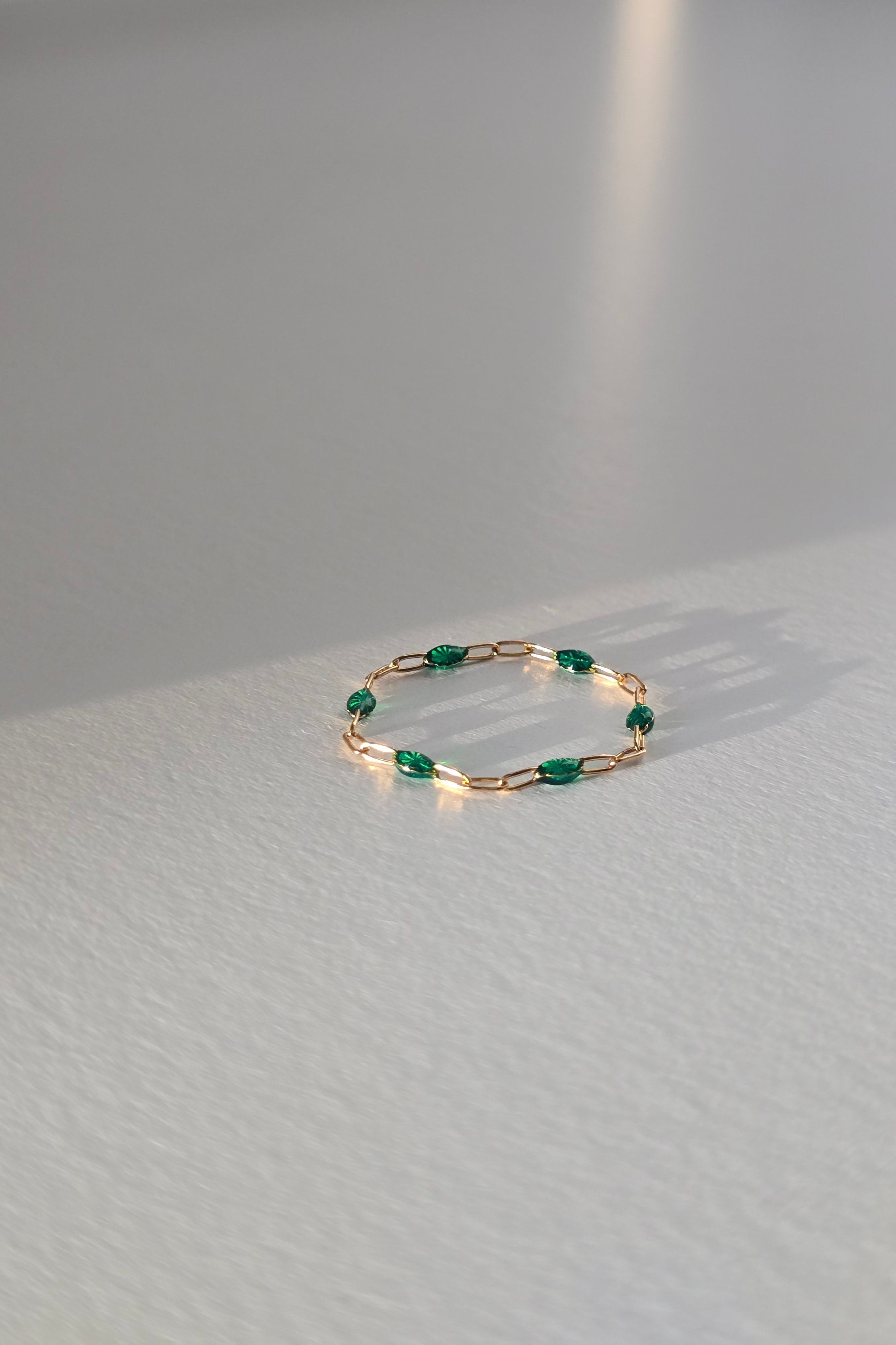 A delicate gold ring with small green gemstone accents, lasting on a light gray textured table.