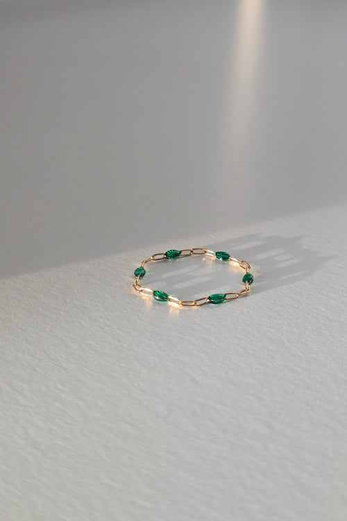 A delicate gold ring with small green gemstone accents, lasting on a light gray textured table.