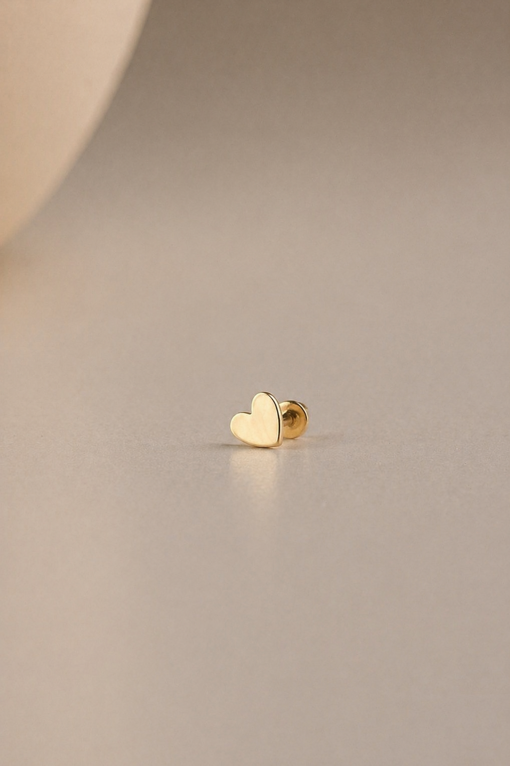 Gold heart-shaped flatback stud on a beige background