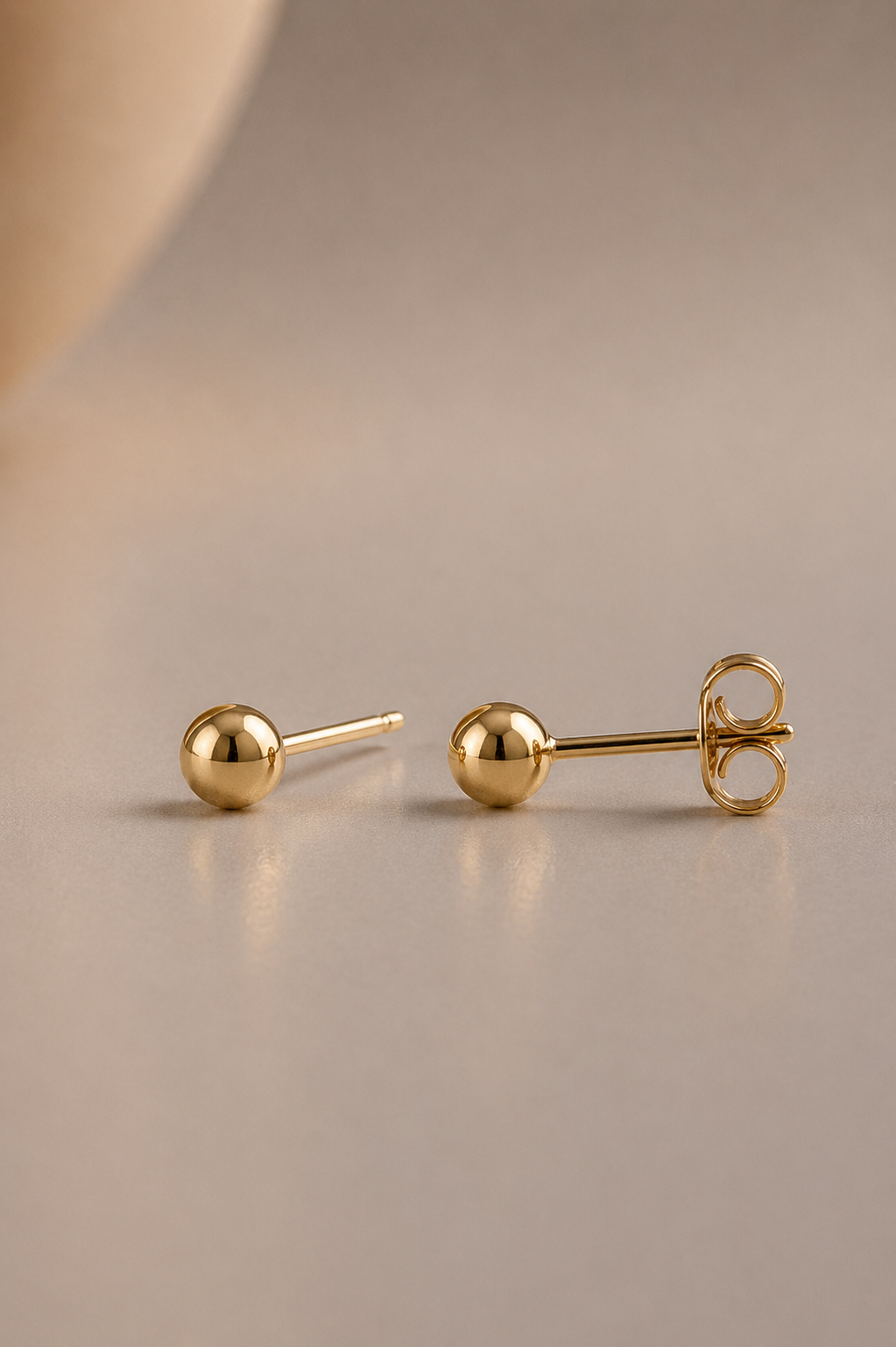 Pair of 14k gold 4mm gold stud earrings on a beige background