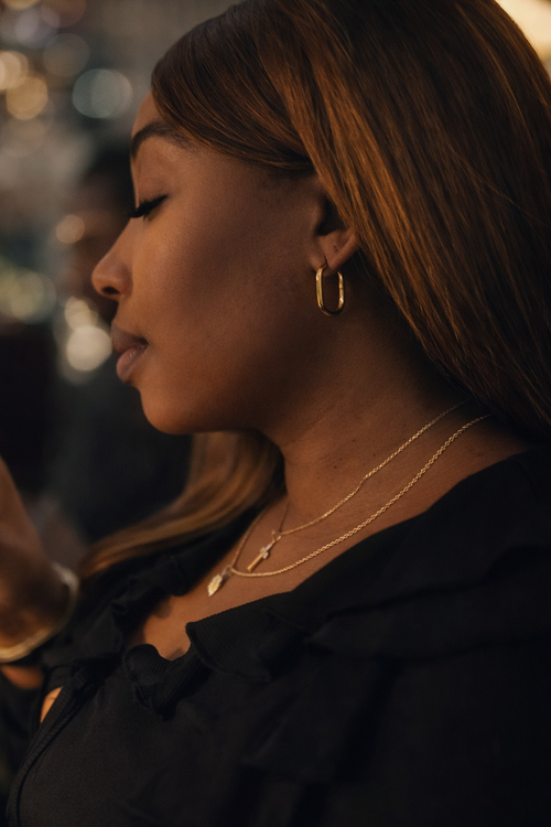 Woman drinking from a glass in a dimly lit setting wear OLANTI earrings 