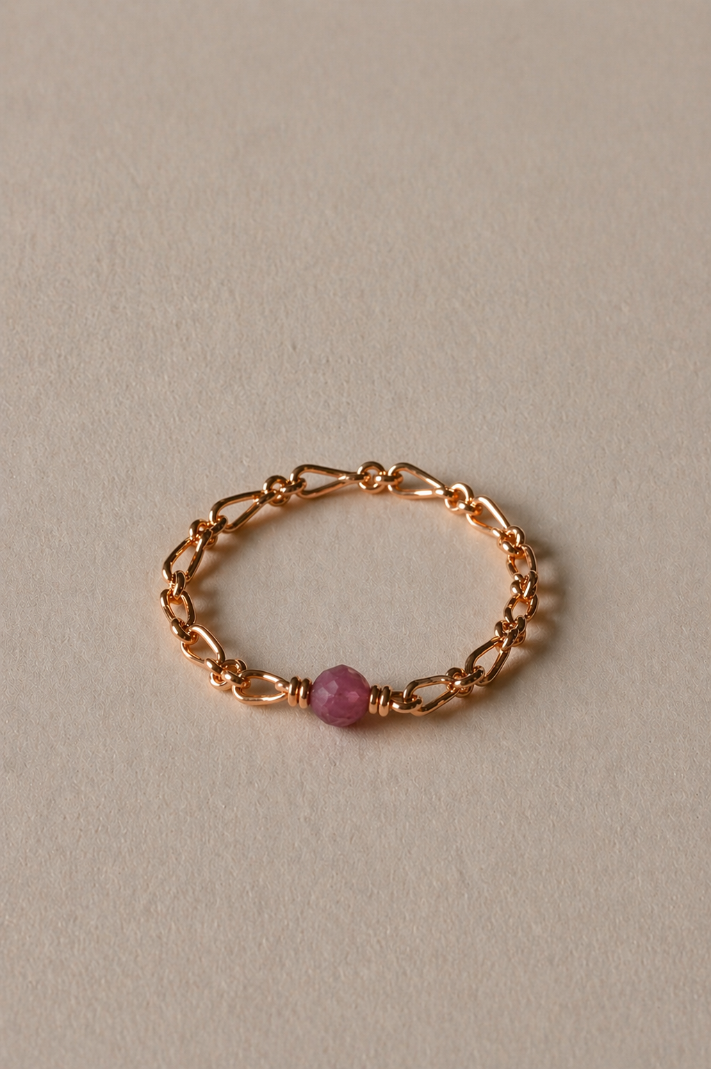 Gold chain ring with a tourmaline gemstone on a beige background