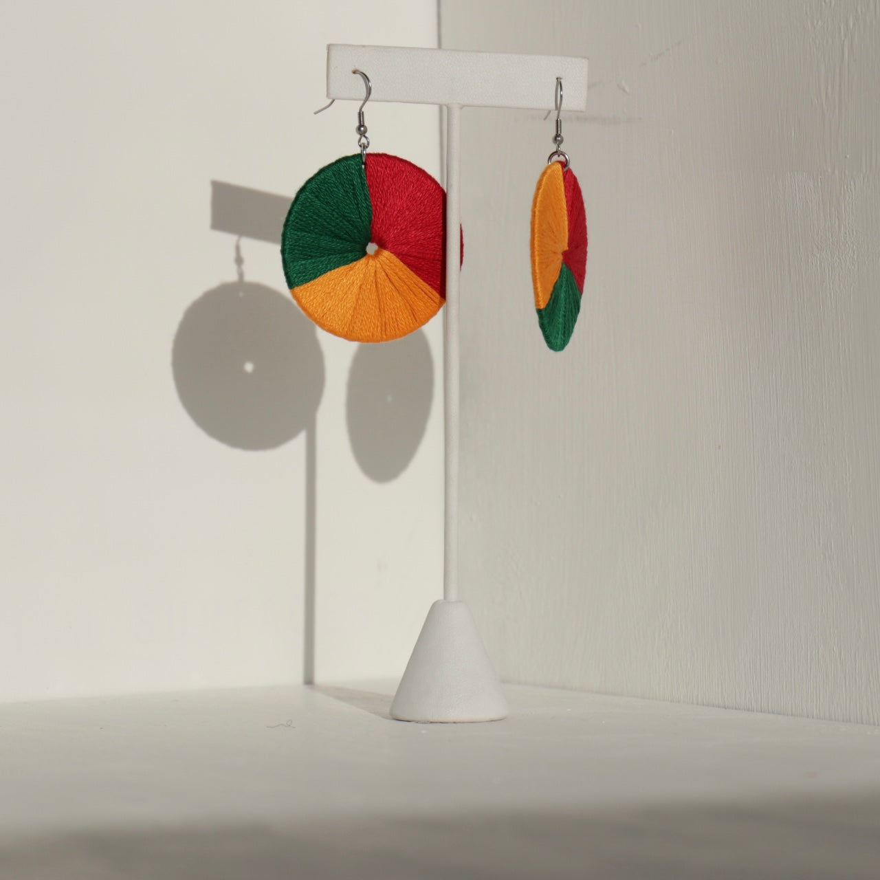 The Bode earrings in green, red, and yellow displayed on a stand with soft lighting