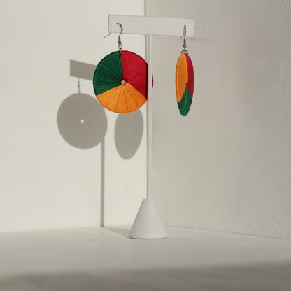 The Bode earrings in green, red, and yellow displayed on a stand with soft lighting