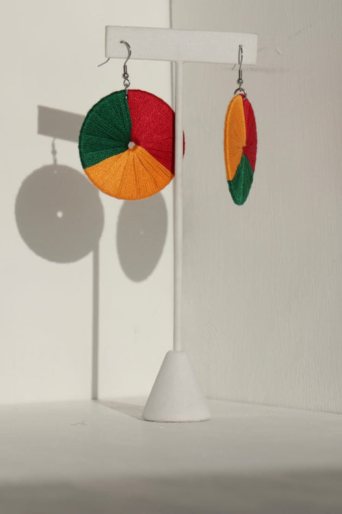 The Bode earrings in green, red, and yellow displayed on a stand with soft lighting