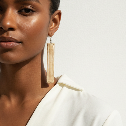 Woman wearing a white top with long earrings against a neutral background