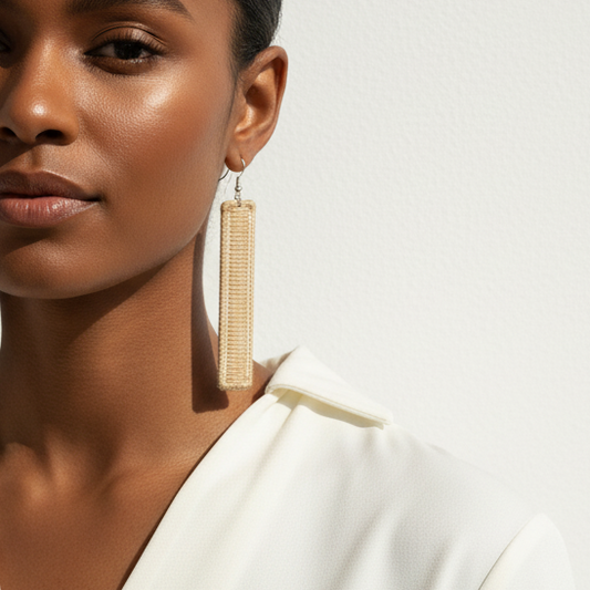 Woman wearing a white top with long earrings against a neutral background