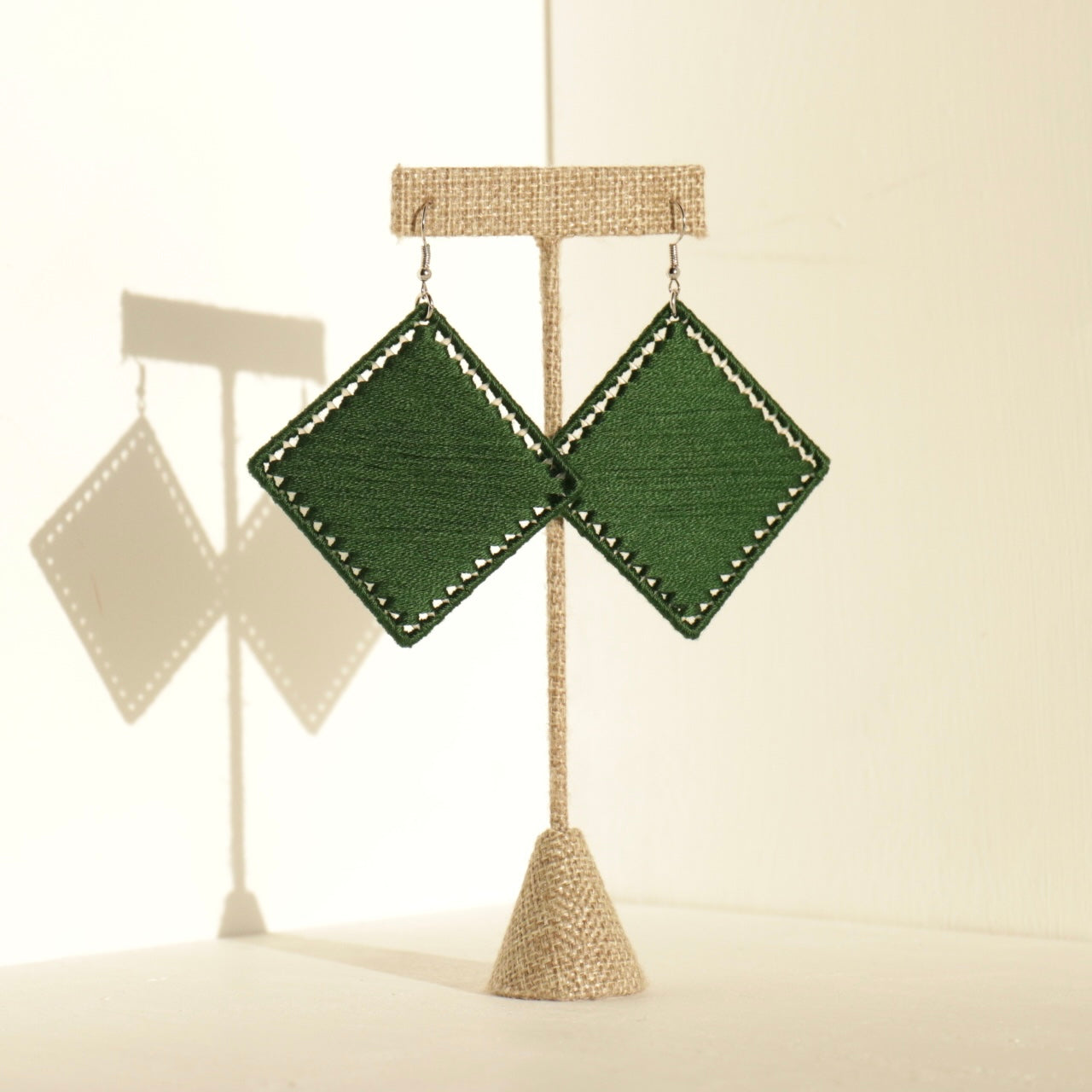Diamond-shaped Kwame earrings in green, resting on a jewelry stand
