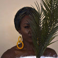 Model wearing The Valente earrings in yellow, partially concealed by palm leaves