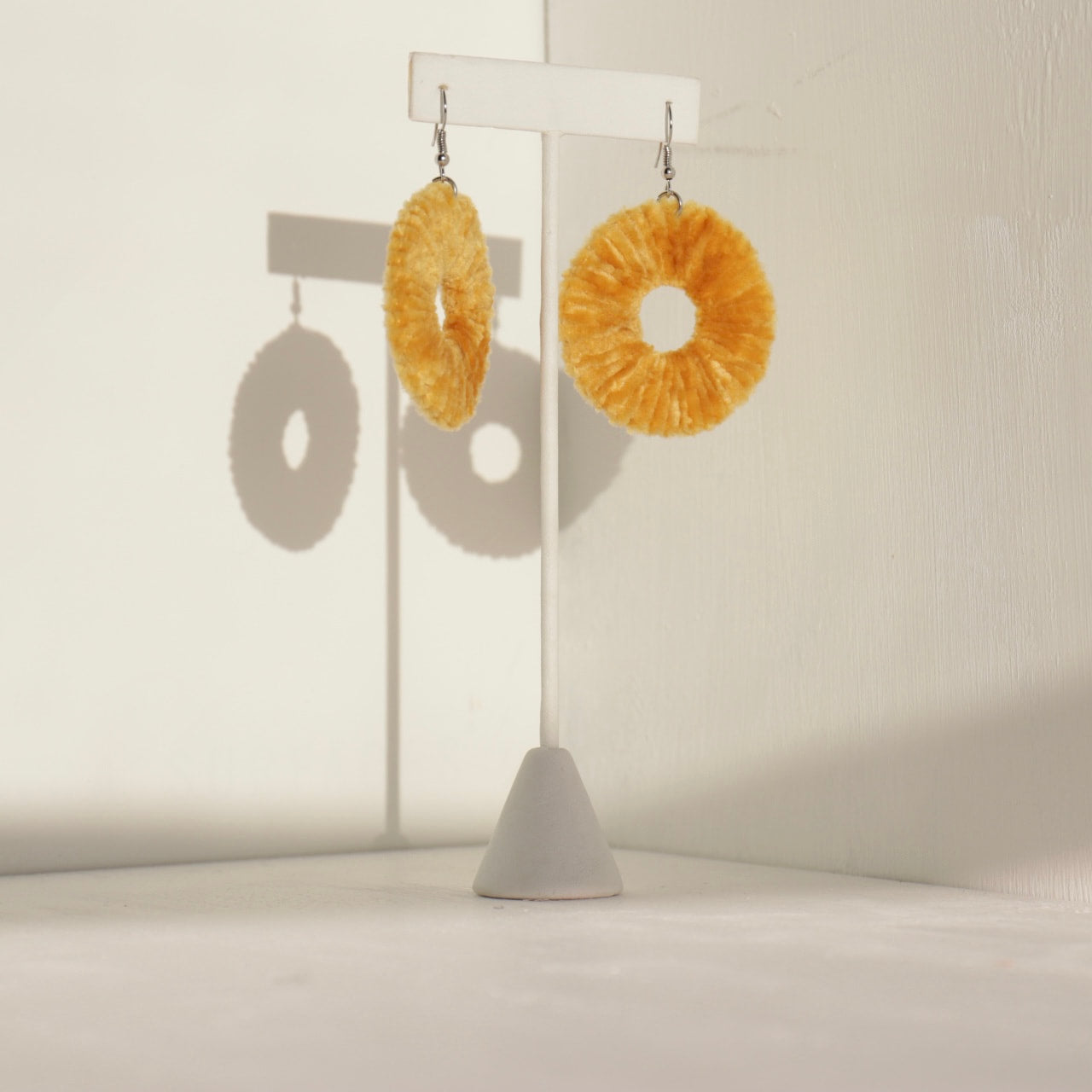 The Vinny statement earrings in a golden hue, displayed on a stand with soft lighting