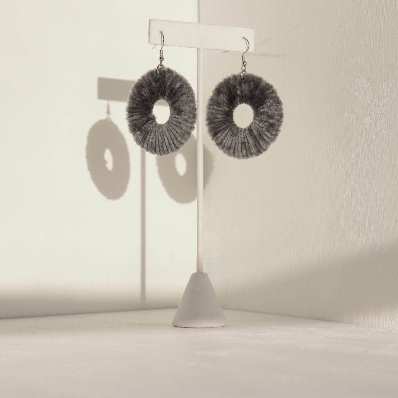 The Vinny earrings in deep charcoal, crafted with intricate texture and displayed on a jewelry stand