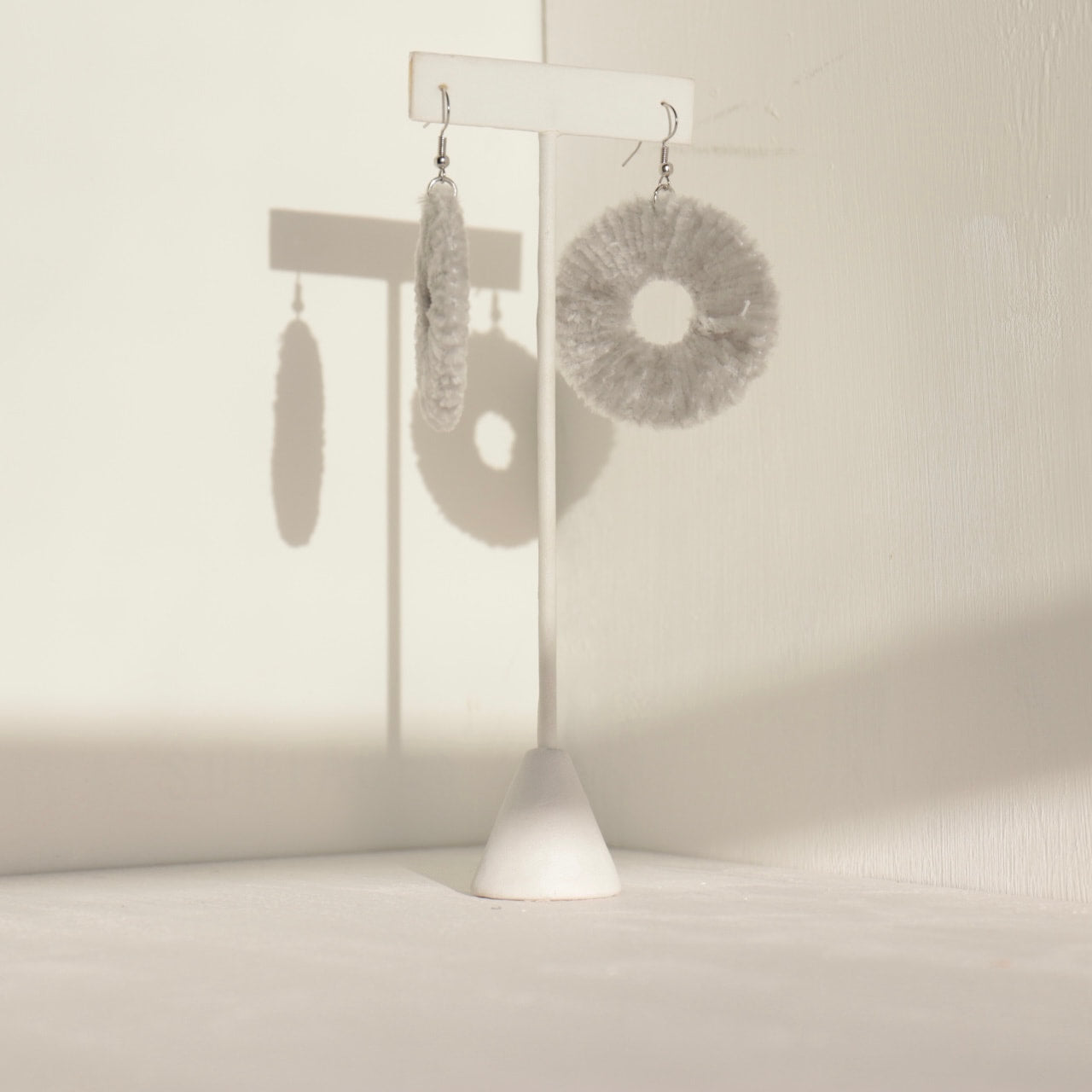 Soft grey Vinny earrings, photographed in a minimalist setting with shadow play.